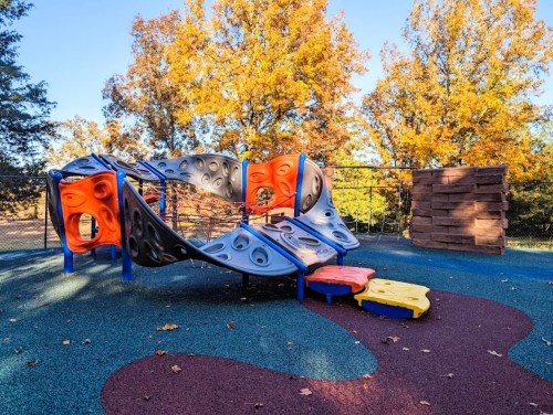 Colorful playground equipment surrounded by autumn trees with orange and yellow leaves.