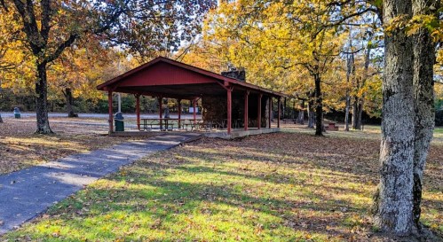 A red picnic shelter surrounded by autumn trees and fallen leaves, with a path leading to it.