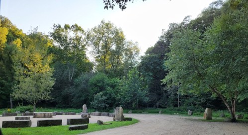 A serene outdoor scene with a dirt path winding through trees and stone markers in a lush green area.