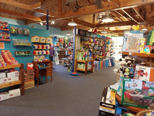 A colorful toy store interior filled with shelves of toys, games, and plush animals under a wooden ceiling.