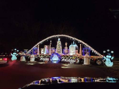 A festive holiday display featuring lights, snowmen, and a "Happy Holidays" sign, set against a night sky.