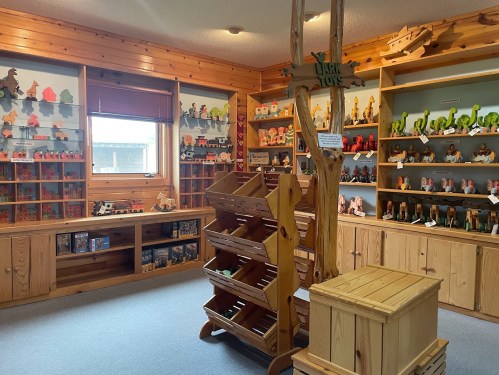 A cozy toy store interior featuring wooden shelves filled with colorful toys and a central display stand.