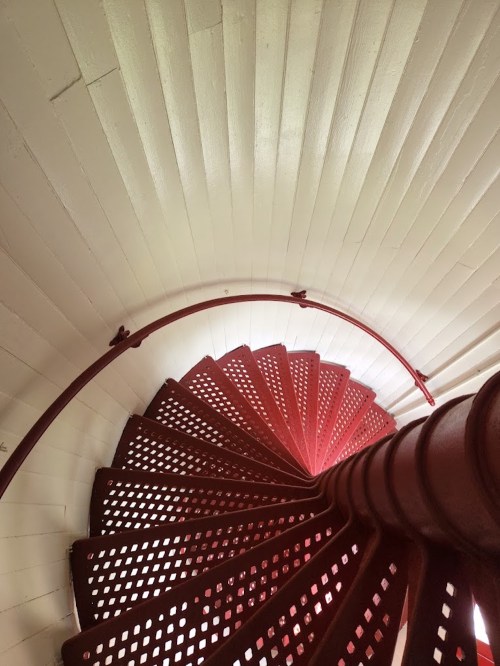Aerial view of a spiral staircase with red metal railings and white wooden walls.
