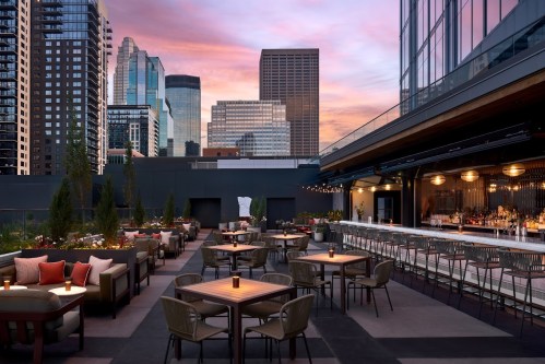 Rooftop bar with tables and chairs, city skyline in the background, and a colorful sunset sky.