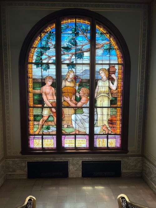 Stained glass window depicting three figures in a natural setting, surrounded by trees and mountains.