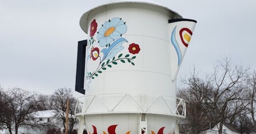 A large, decorative water tower shaped like a coffee pot, featuring colorful floral designs against a gray sky.