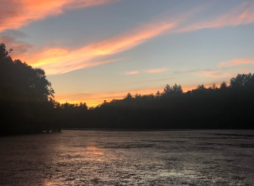 A serene lake at sunset, with colorful clouds reflecting on the water and silhouettes of trees along the shore.