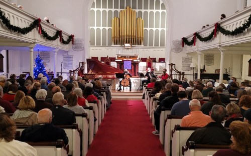 A crowded church interior during a concert, featuring musicians on stage and festive decorations, including a Christmas tree.