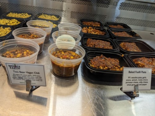 Containers of two bean vegan chili and baked fusilli pasta displayed in a food service area.