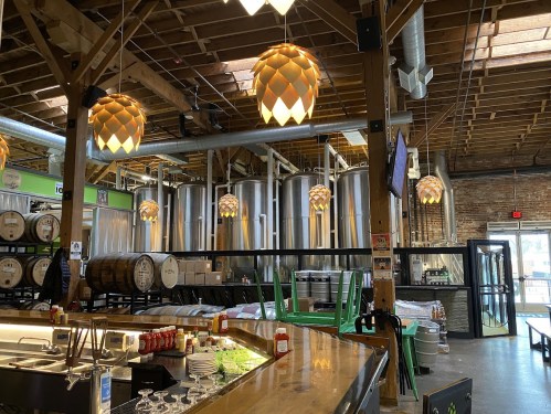 Interior of a brewery featuring large fermentation tanks, wooden barrels, and unique pendant lighting.