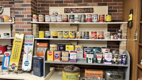 A display of vintage cans and containers on shelves, featuring various brands and colorful labels in a brick setting.