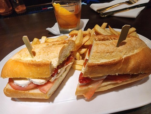 A sandwich with ham, cheese, and tomatoes, served with fries and a drink with a lemon slice on the side.
