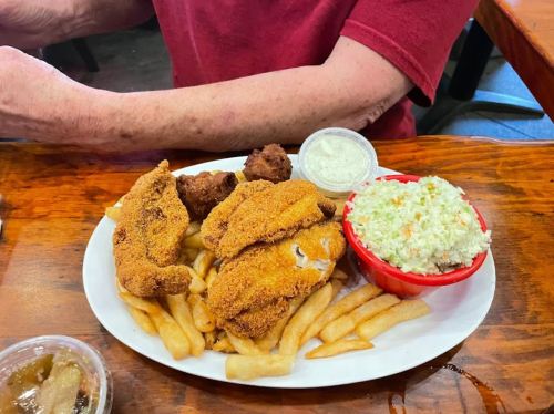 A plate of fried chicken, coleslaw, fries, and hushpuppies on a wooden table.