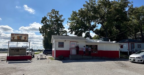 A small, red and white building with a sign for "Big Dave's" and outdoor seating, set against a cloudy sky.
