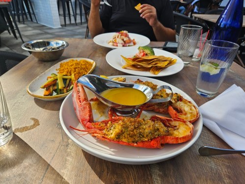 A table with a seafood platter featuring lobster, a bowl of vegetables, and a dessert plate in a restaurant setting.