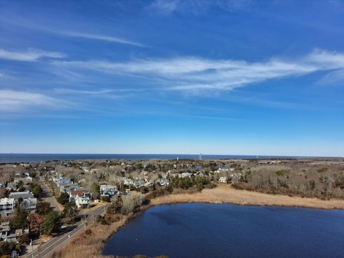 Aerial view of a coastal town with houses, a lake, and a clear blue sky in the background.