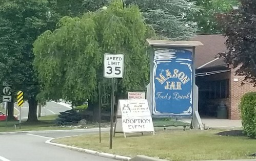 Sign for Mason Jar Food & Drink with a speed limit sign and an advertisement for a Sunday brunch and adoption event.