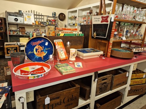 A vintage display featuring retro items, including trays, books, and glassware, on a red table in a quaint shop.