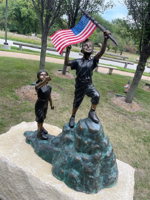 A bronze sculpture of two children, one holding an American flag, standing triumphantly on a rock.