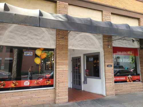 Exterior of Bun Burger restaurant with open sign, balloons, and large windows displaying the menu.