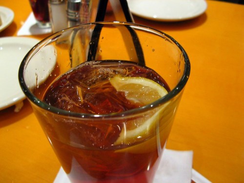 A close-up of a glass filled with iced tea and a slice of lemon, resting on a napkin on a wooden table.