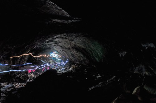 A dark cave interior with colorful light trails illuminating the rocky walls and ground.