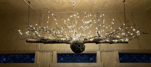 A unique chandelier made of a branch with twinkling lights, suspended from the ceiling in a cozy interior.