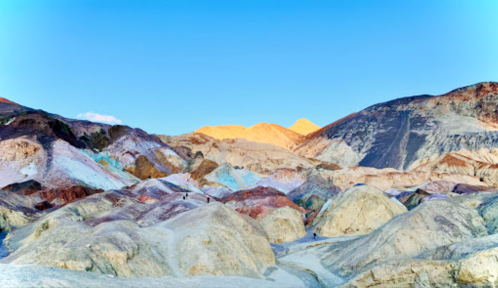 Colorful, rugged mountains under a clear blue sky, with sunlight illuminating the peaks in the background.