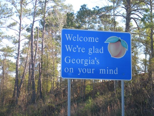 Welcome sign featuring a peach, stating "We're glad Georgia's on your mind" amidst trees.