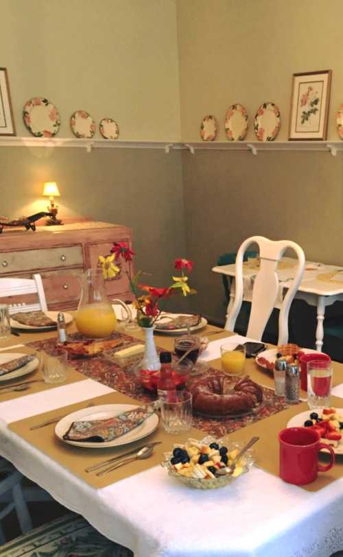 A beautifully set dining table with a floral tablecloth, plates, drinks, and a variety of breakfast foods.