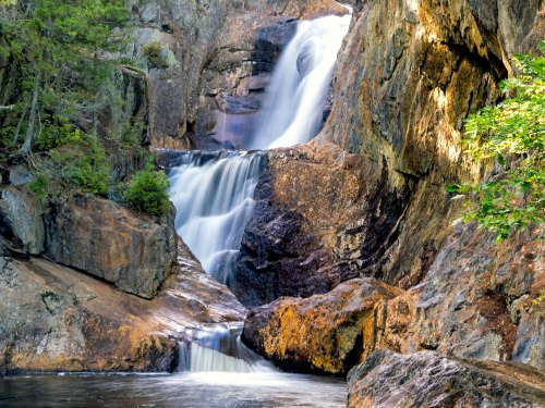 A serene waterfall cascading over rocky cliffs, surrounded by lush greenery and a tranquil pool below.