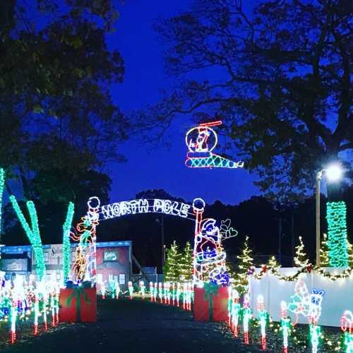 Colorful holiday lights decorate a pathway, featuring a sign for "North Pole" and a helicopter in the night sky.