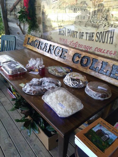 A wooden sign for LaGrange College beside a table displaying various homemade desserts and books.