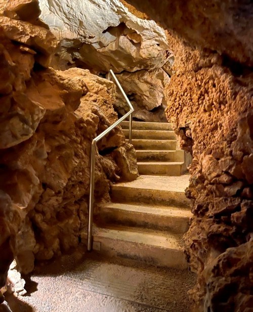 A winding staircase leads through a rocky cave, surrounded by textured stone walls and natural formations.