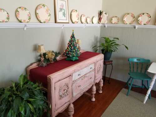 A cozy room with a vintage sideboard, a small decorated Christmas tree, plants, and decorative plates on the wall.