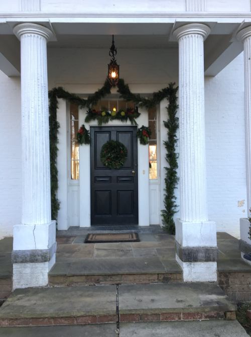 A festive front door adorned with a wreath and greenery, flanked by white columns and a lantern above.