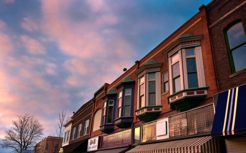 Historic storefronts with colorful bay windows under a pastel sky at sunset.