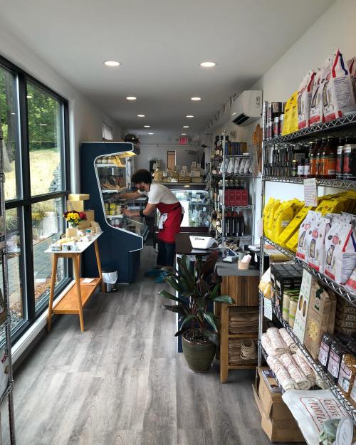 A cozy shop interior with shelves of products and a person in an apron preparing items at a display case.