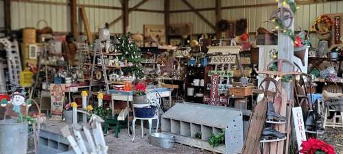 A cozy antique shop filled with various vintage items, furniture, and holiday decorations in a rustic barn setting.
