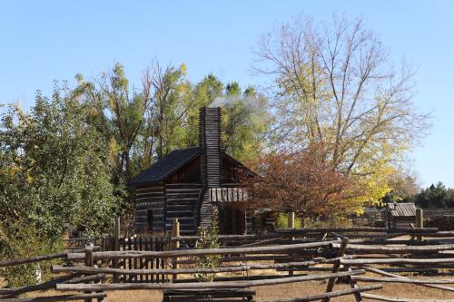 A rustic log cabin with smoke rising from the chimney, surrounded by trees and a wooden fence in autumn.