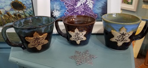 Three ceramic mugs in varying colors, each featuring a star design and the text "Written in the Stars."