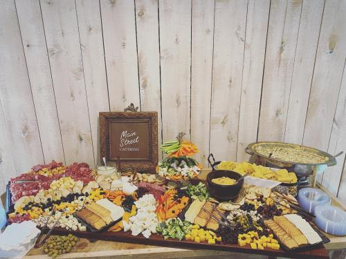 A beautifully arranged catering spread featuring cheeses, meats, fruits, crackers, and a decorative sign on a wooden backdrop.
