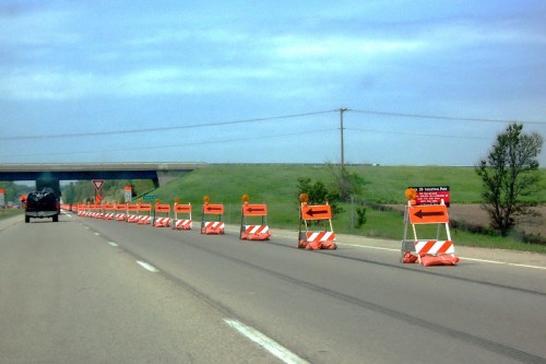 Road construction ahead with orange barriers and directional signs on a highway under a cloudy sky.