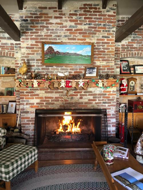Cozy living room with a brick fireplace, festive decorations, and a painting of mountains above the mantel.