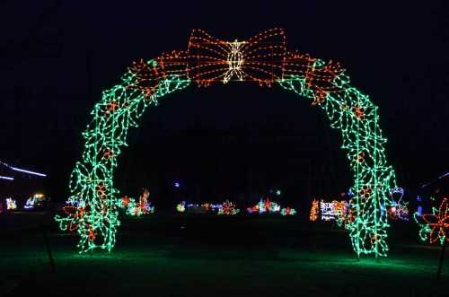 A festive arch made of green and orange lights, adorned with a large bow, set against a dark night sky.