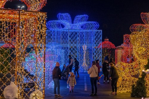 A festive display of illuminated gift boxes and decorations, with families exploring the colorful lights at night.