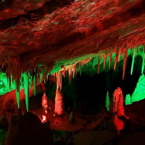 Colorful cave interior with stalactites and stalagmites illuminated in red and green lights.