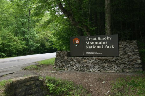 Sign for Great Smoky Mountains National Park, surrounded by lush greenery, near a quiet road.