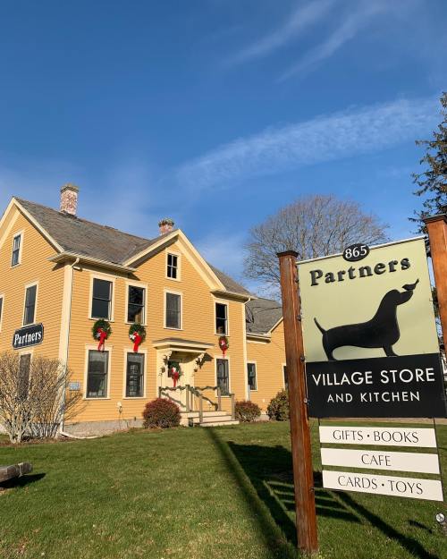 A yellow house with festive decorations, featuring a sign for "Partners Village Store and Kitchen" in front.
