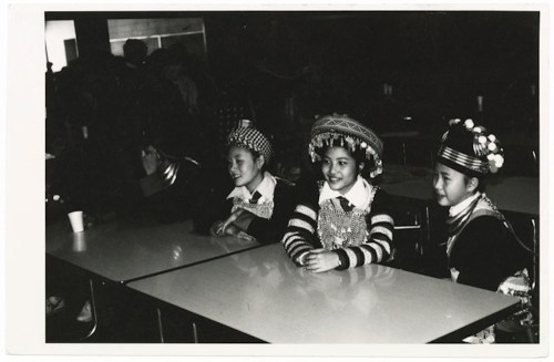 Three girls in traditional attire sit at a table, smiling, in a black-and-white photo.